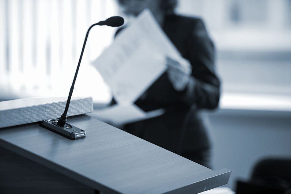 Microphone on a podium, with woman preparing a speech in the background 