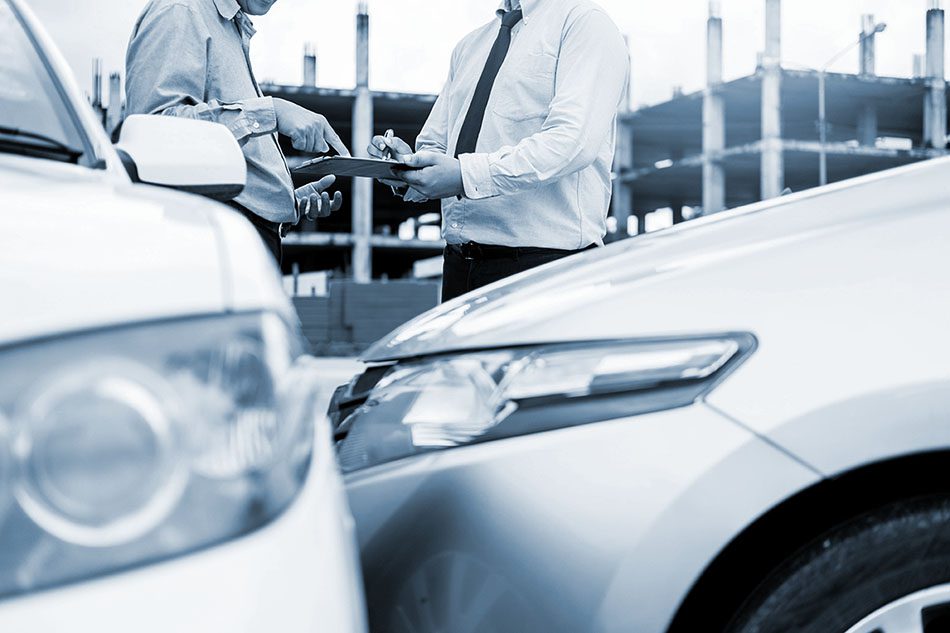 Insurance agent writing on clipboard while examining car after accident claim being assessed and processed