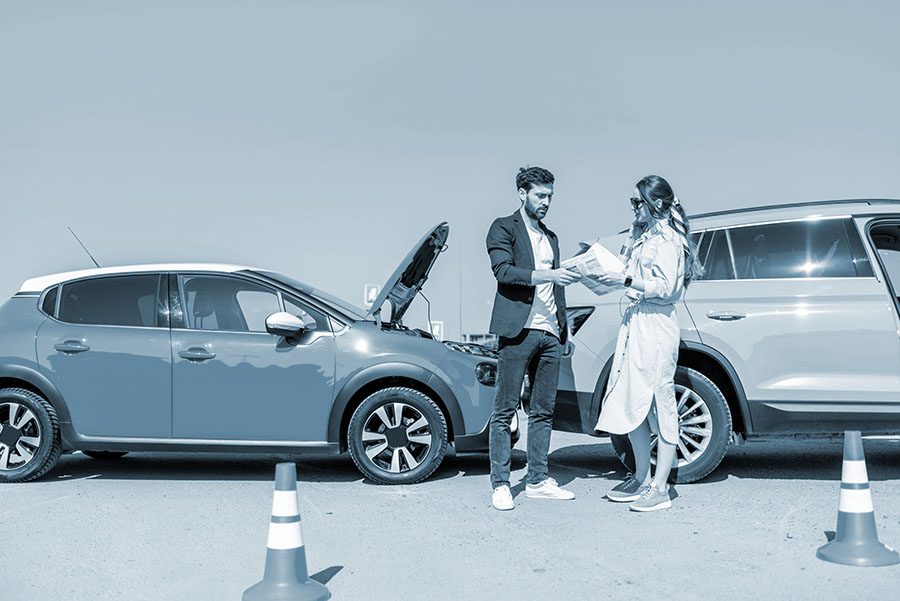 Man and woman arguing, standing together on the road with their cars on the background after the car accident